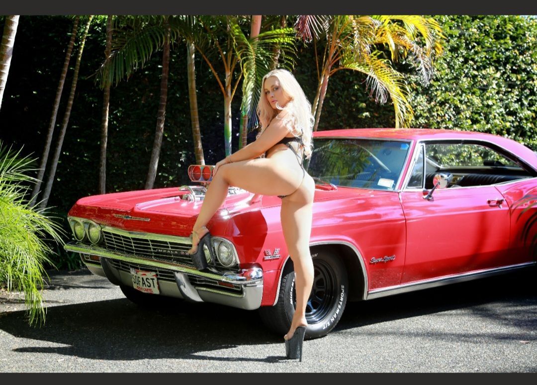 Woman posing on a red classic car in a tropical driveway