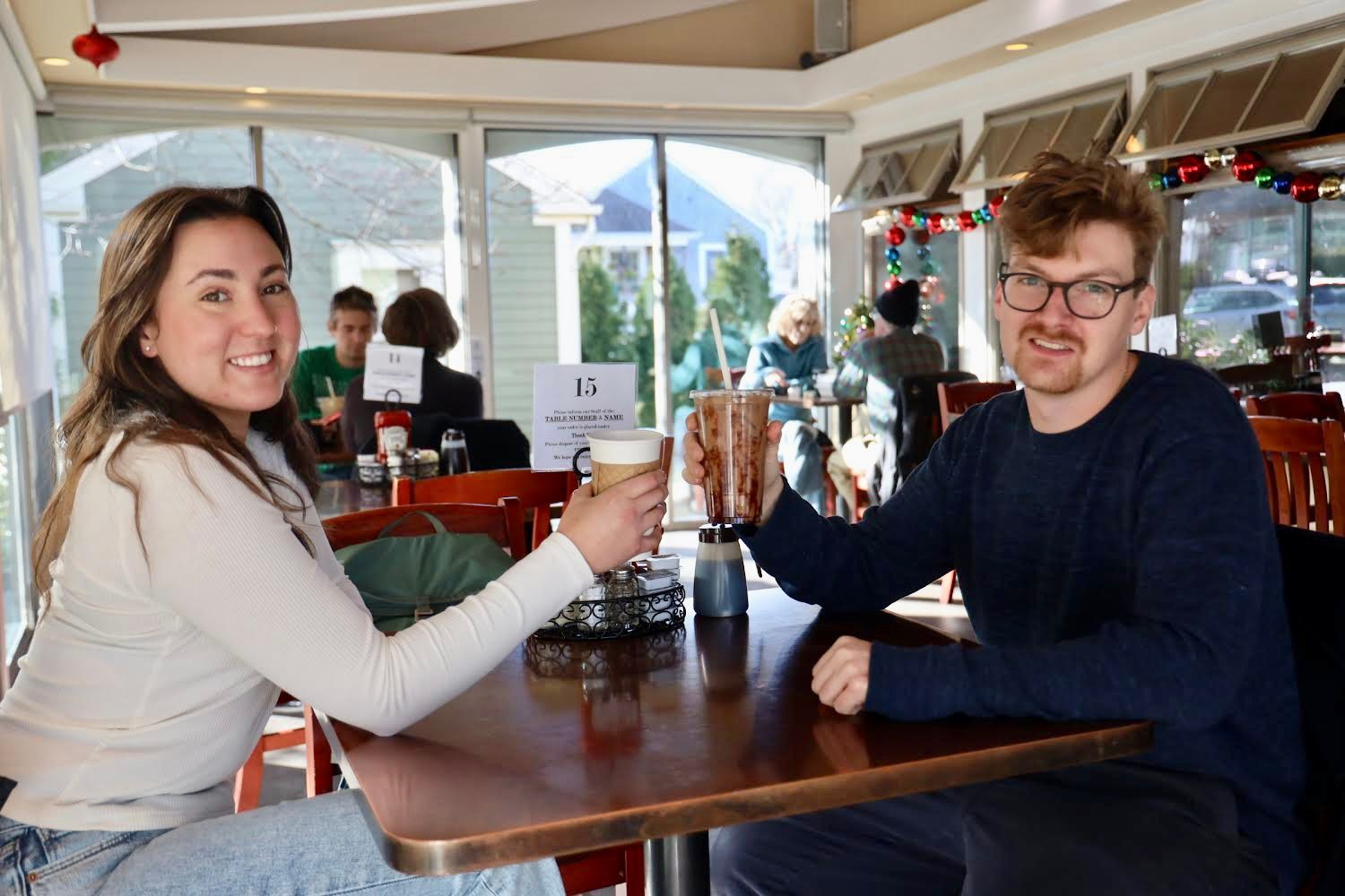 Two people toasting coffees at a cafe table.