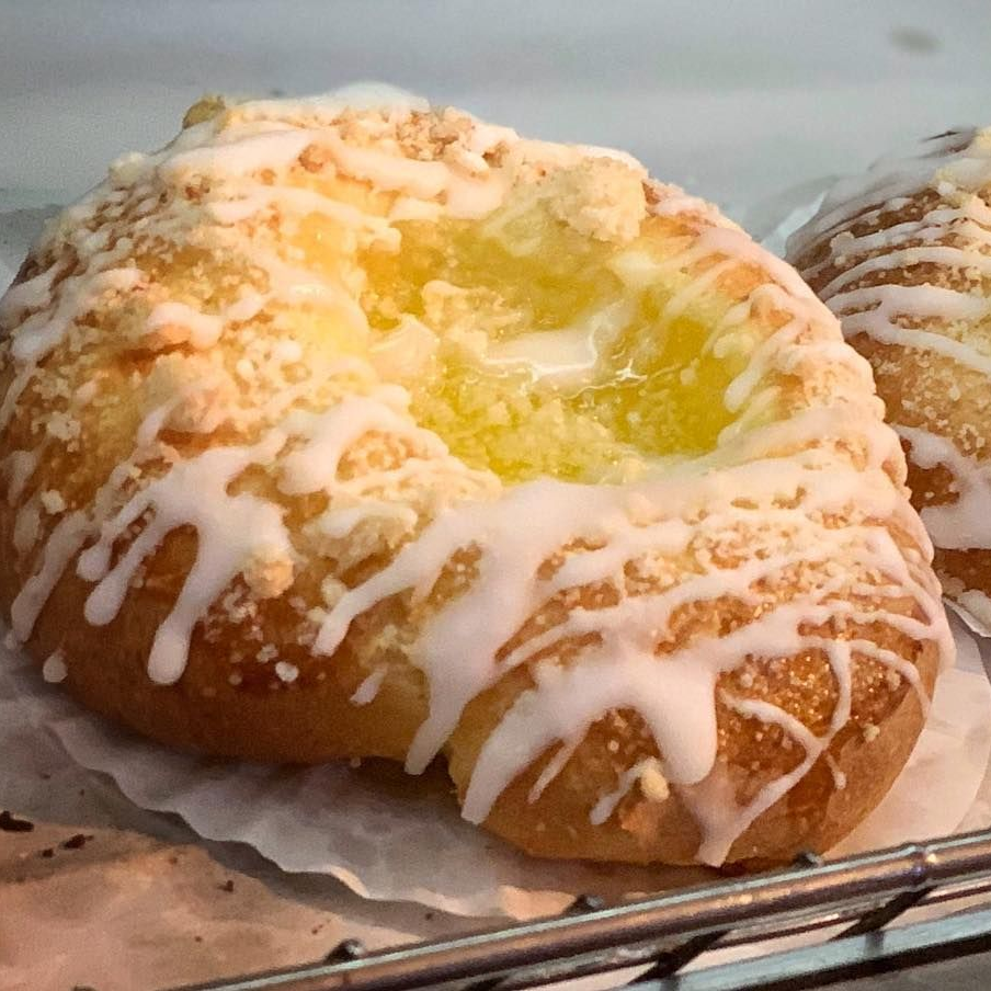 A golden-brown danish pastry topped with yellow fruit filling, streusel crumbles, and a drizzle of white icing.