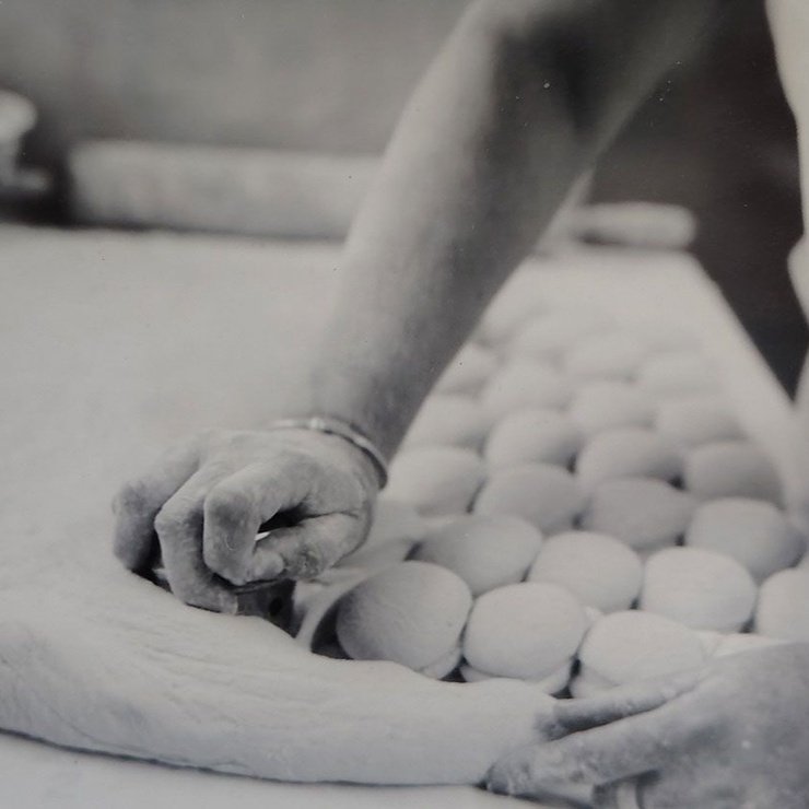 A close-up of a person using a round cutter to shape small, uniform circles from a large, flat piece of dough.