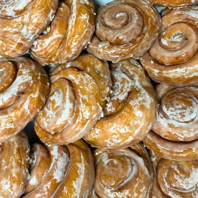 A close-up view of multiple glazed cinnamon rolls packed closely together, showing their swirl patterns and shiny coating.