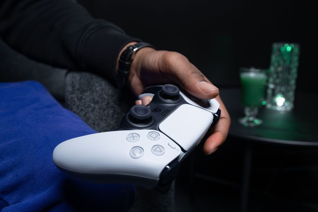 Hand holding a white game controller near a lit gaming setup with a green drink in the background