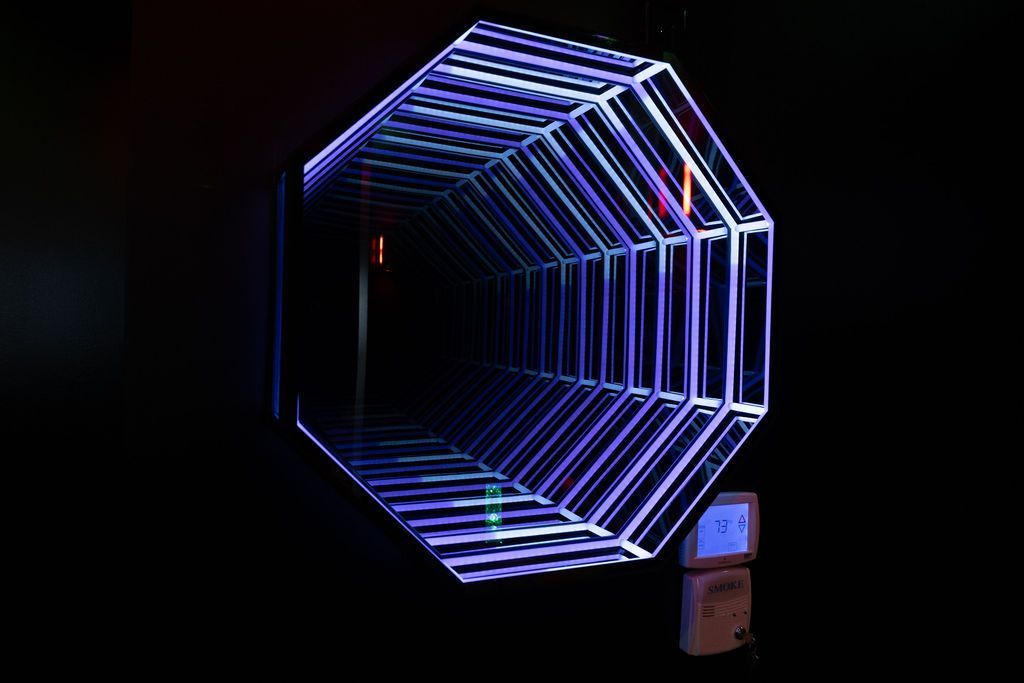 Neon purple-blue geometric tunnel of glowing light tubes against a dark background, with a small phone below