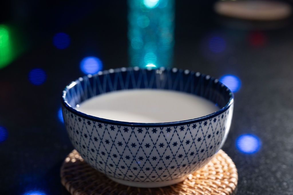 Blue-and-white patterned ceramic bowl on a woven coaster, with blurred colorful lights in the background