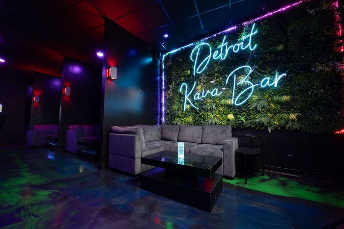 Neon-lit lounge interior with gray booths, dark walls, and a glowing “Detroit Kava Bar” sign