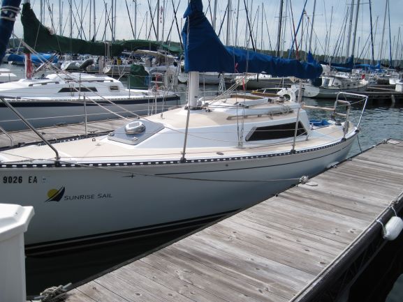 Sailboat docked at a marina with blue sail up. White hull, wooden dock.