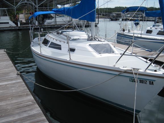 White sailboat with blue sails docked at a marina.