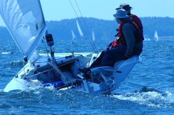 Sailboat heeling in choppy water, two people on board, other sailboats in background.