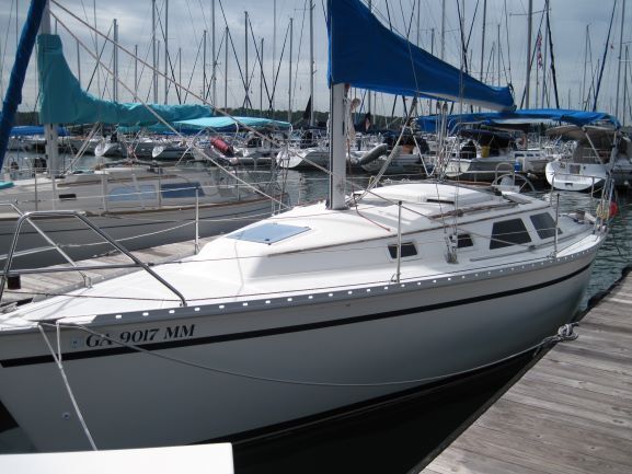 White sailboat at a marina, blue sail, cloudy sky.