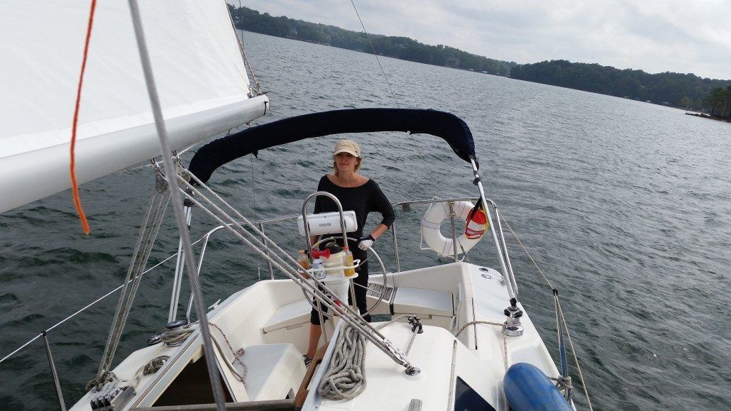 Woman piloting a sailboat on a lake with a blue canopy.
