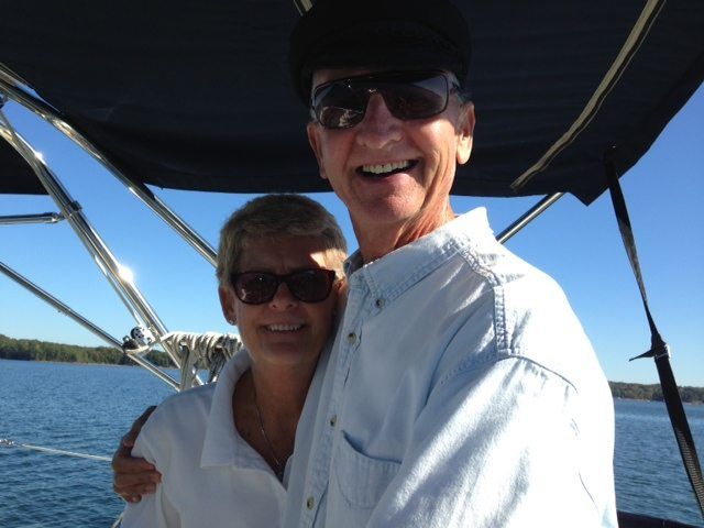 Couple smiling, embracing on a boat, blue water, sunny day, one wearing sunglasses and a hat.