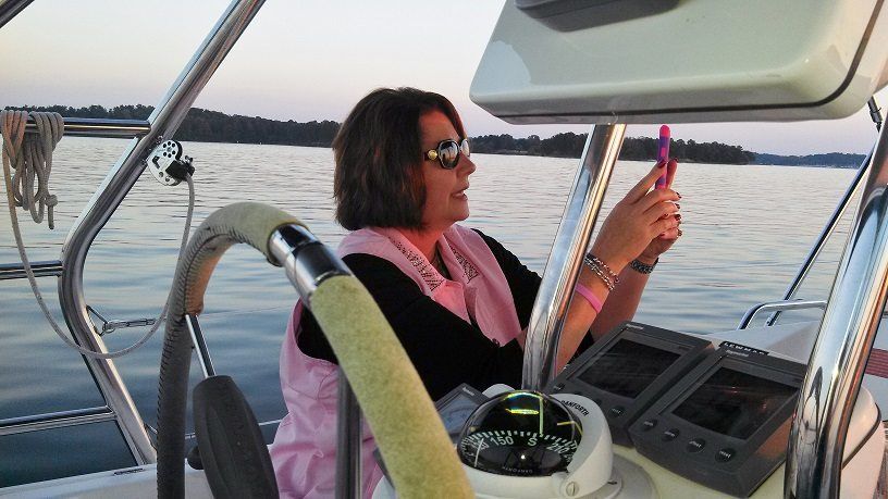 Woman on sailboat taking a photo of the water. Wearing sunglasses and pink vest.