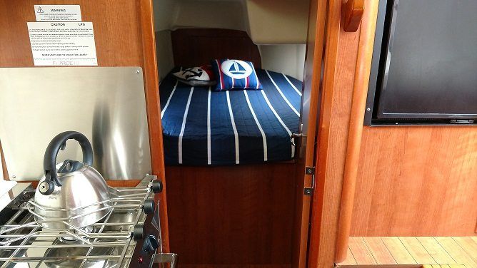 Cabin interior with bed, stove, and TV. Bed has blue and white striped blanket.