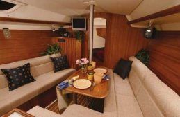 Interior of a sailboat cabin, with wood paneling, seating, and a table set for a meal.
