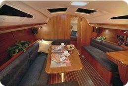 Interior of a sailboat with wooden paneling, blue seating, table set with place settings, and overhead skylights.