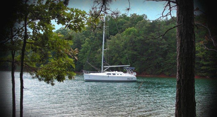Sailboat on a lake, surrounded by green trees and foliage.
