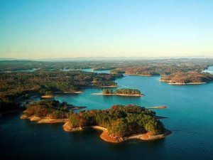 Lush, forested islands dot a serene, blue lake under a clear sky.