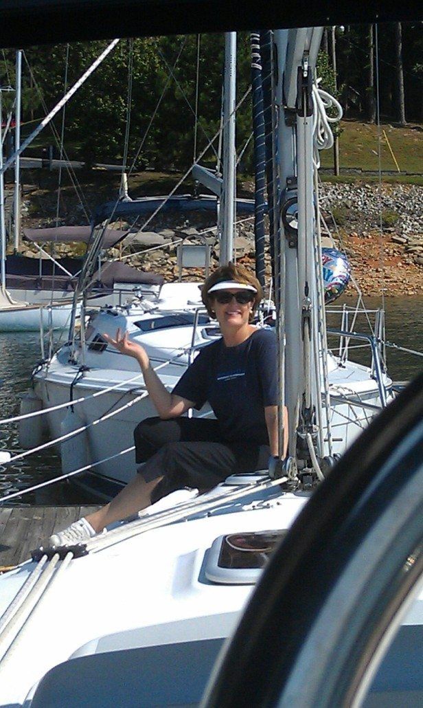 Woman on sailboat, smiling, gesturing. Boat on water at dock.