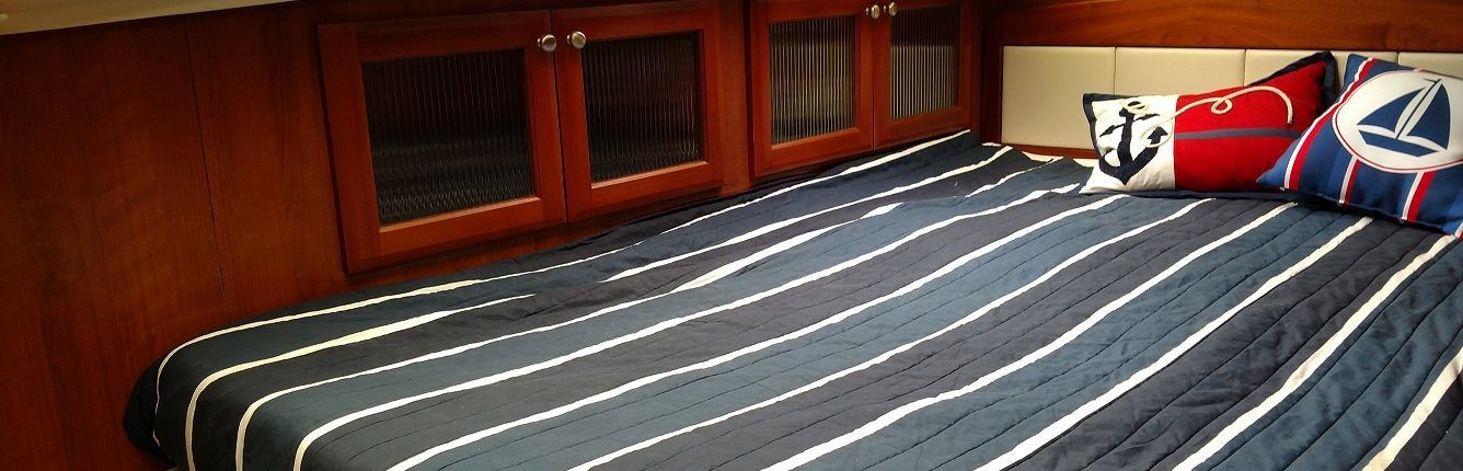 A cabin bed with a striped comforter and nautical pillows under wooden cabinets.
