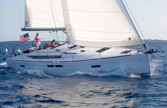 Sailboat on the water with sails up; people on deck near an American flag.