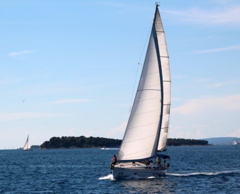 Sailboat sailing on blue water near an island on a sunny day.
