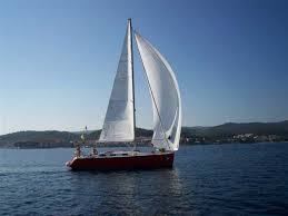 Red sailboat with white sails on a blue sea under a clear sky.