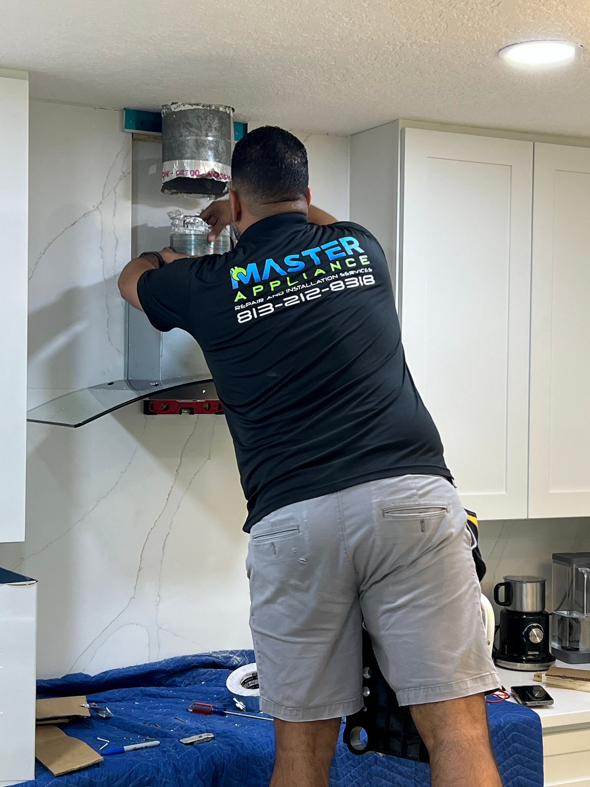 A man in a black shirt is working on a kitchen hood.