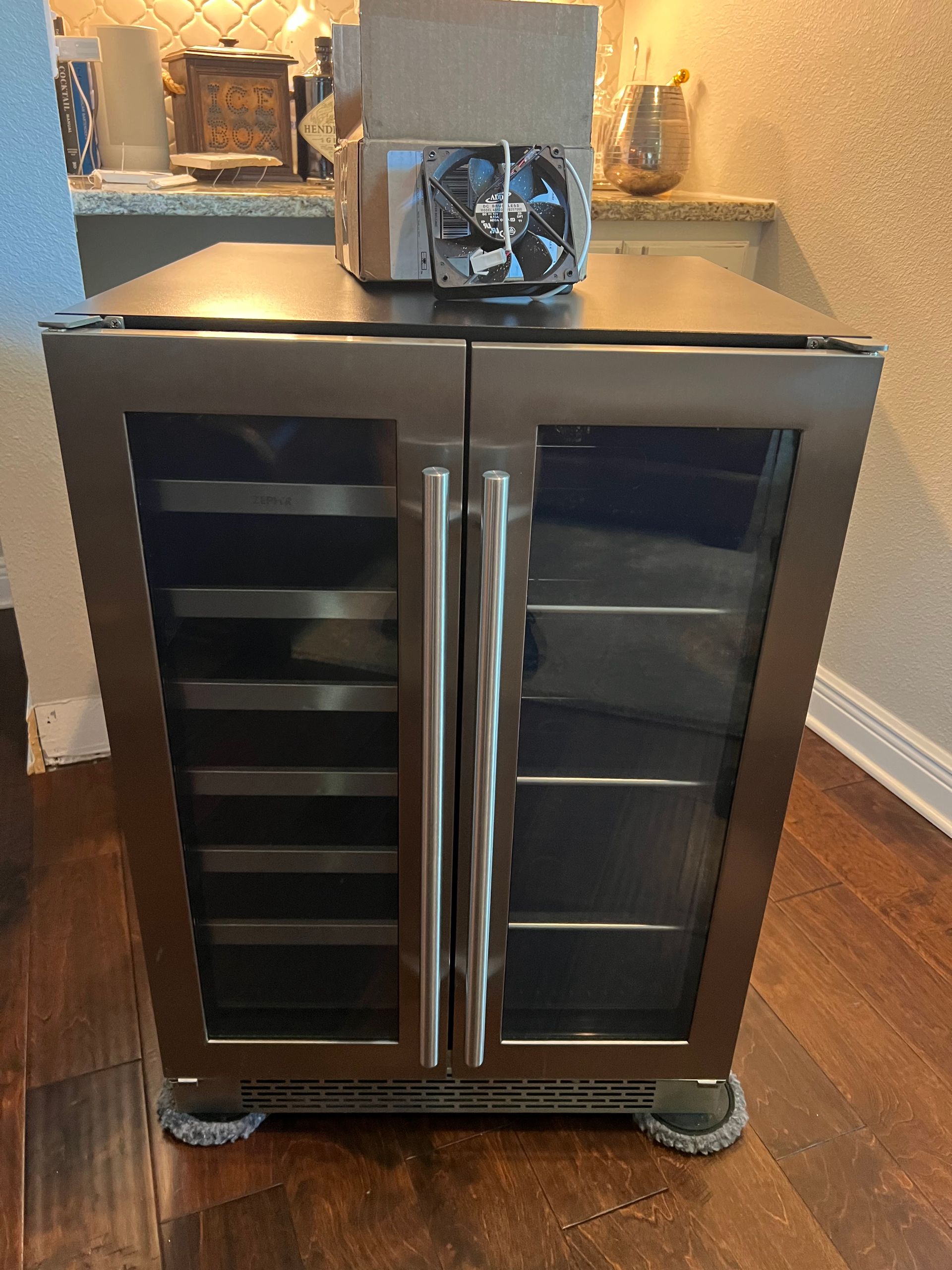 A stainless steel wine cooler is sitting on a wooden floor in a kitchen.