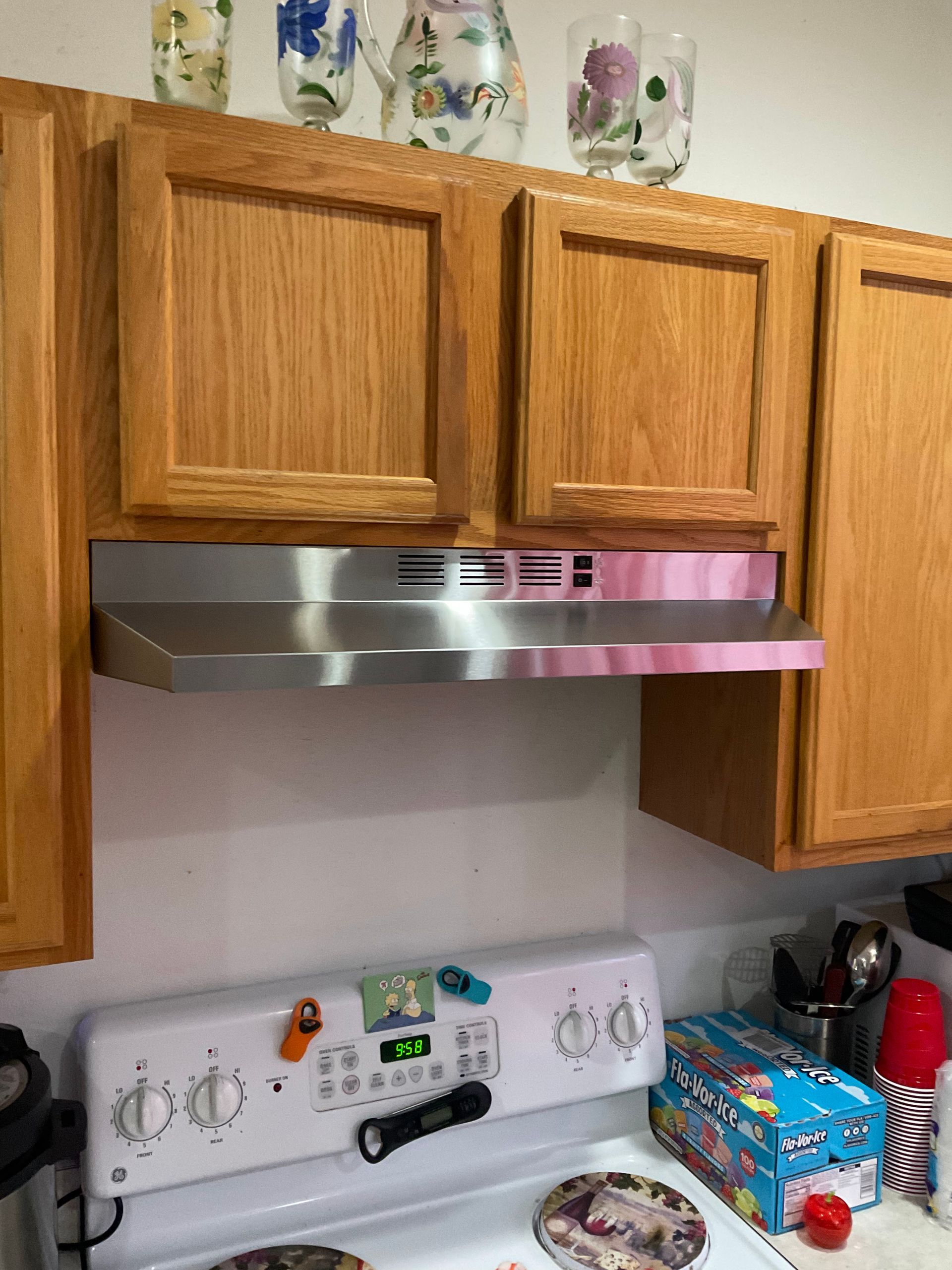 A kitchen with wooden cabinets and a stove with a pink hood.