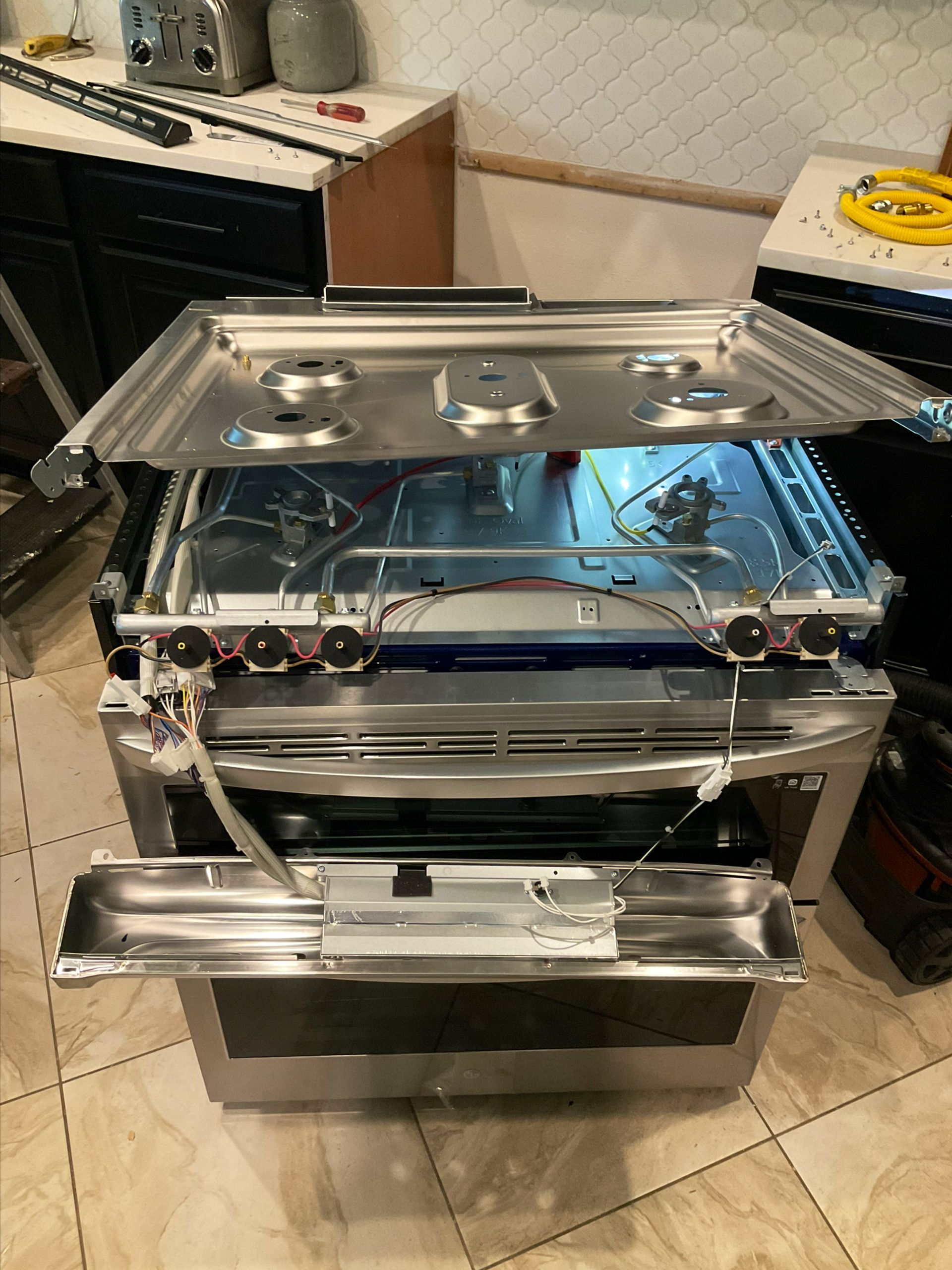 A stove is being repaired in a kitchen with the door open.