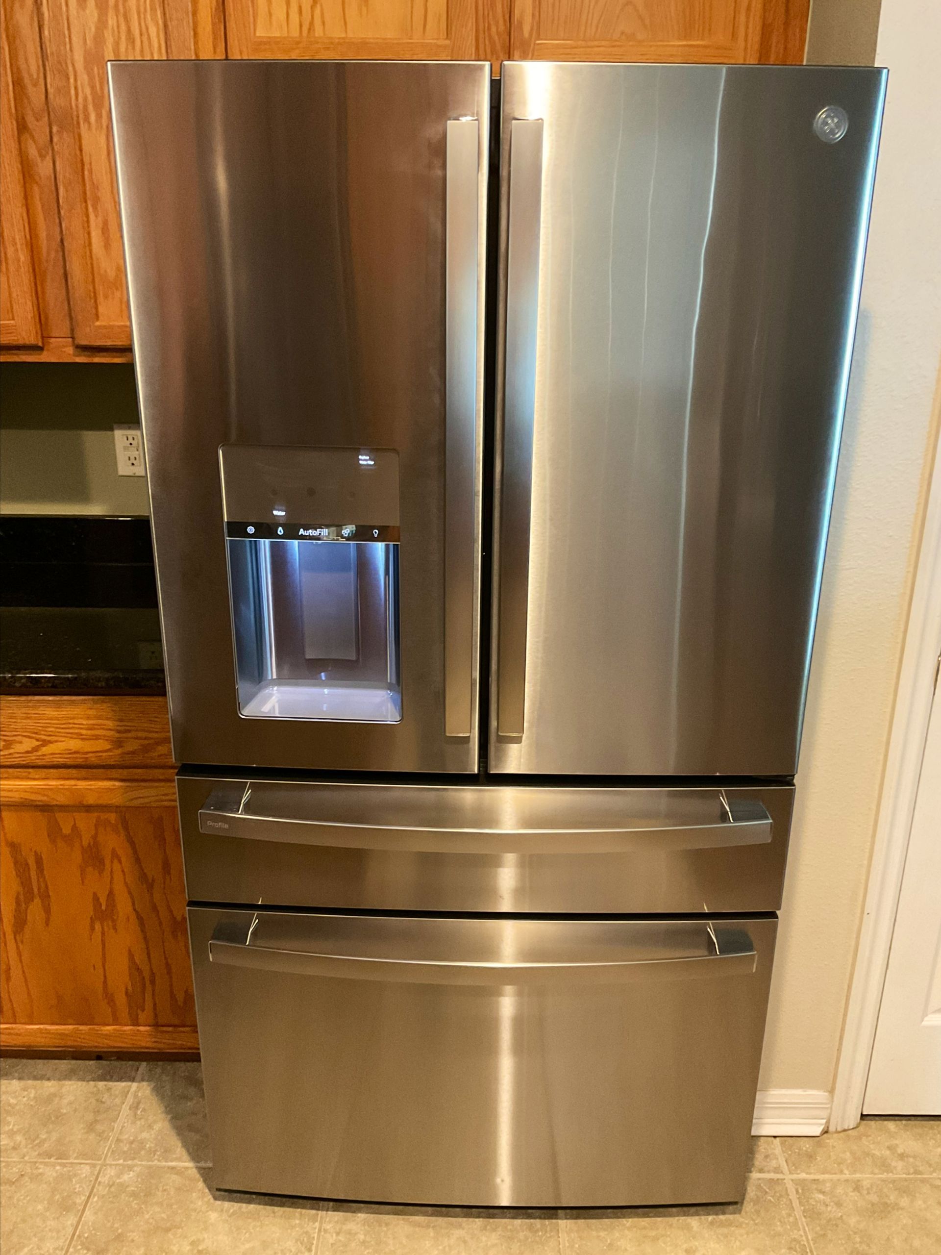 A stainless steel refrigerator is sitting on a tiled floor in a kitchen.