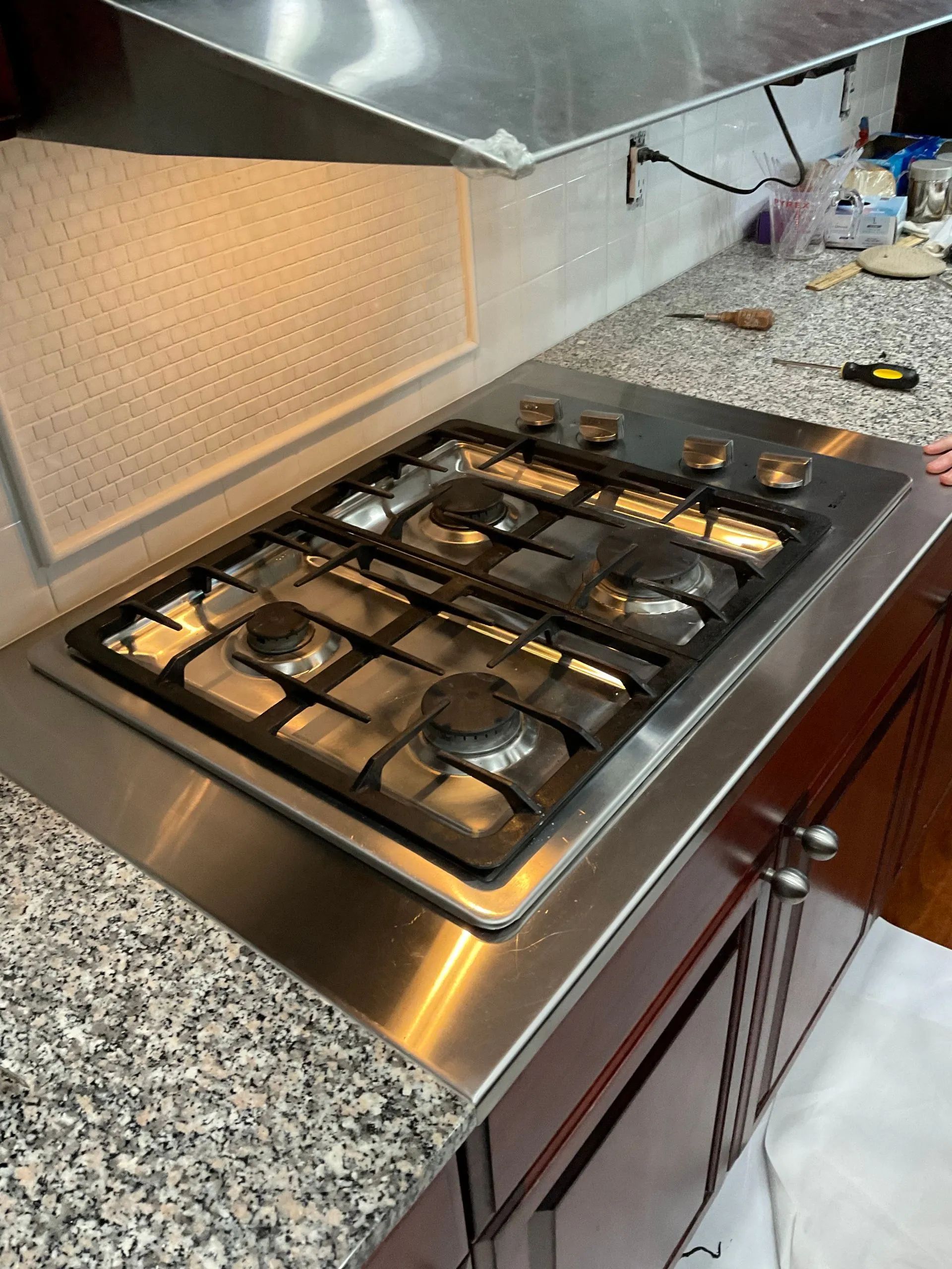 Stainless steel stovetop inset in granite countertop above dark wood cabinets.