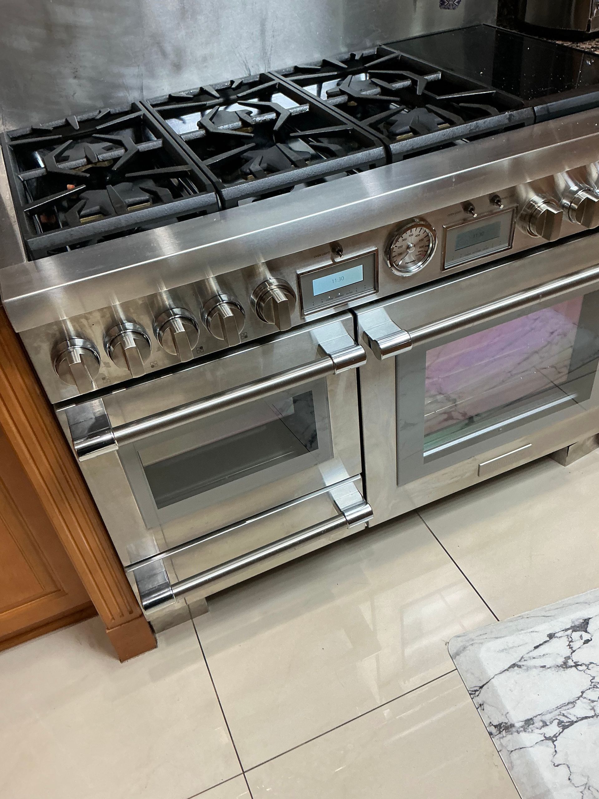 A stainless steel stove top oven is sitting on a tiled floor in a kitchen.