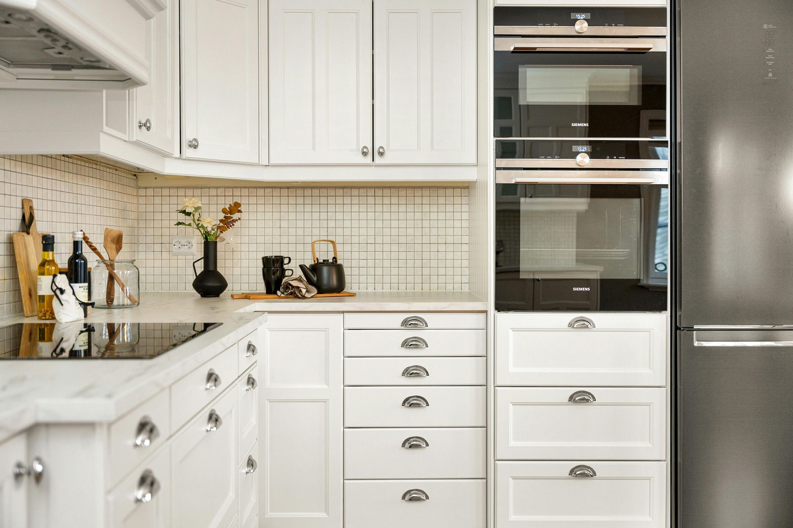 White kitchen with oven, drawers, and a stainless steel refrigerator.