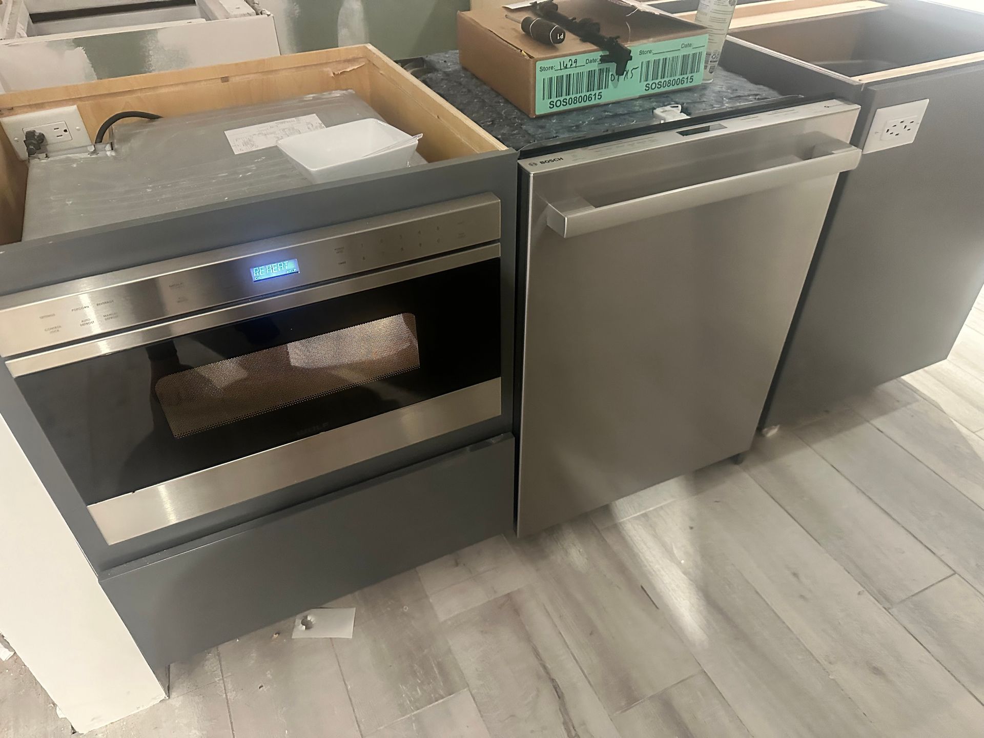 A stainless steel oven and dishwasher are sitting on a wooden floor.