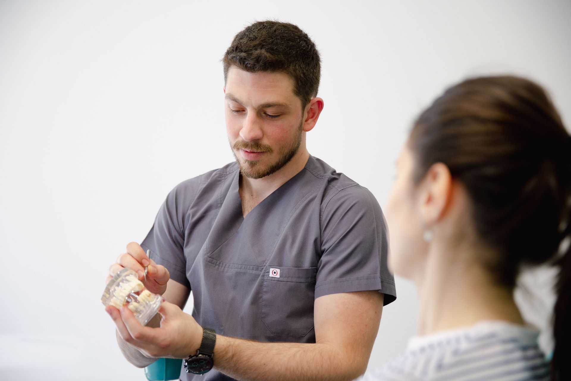 Man demonstrating a hand exercise with a woman watching in a bright clinical setting