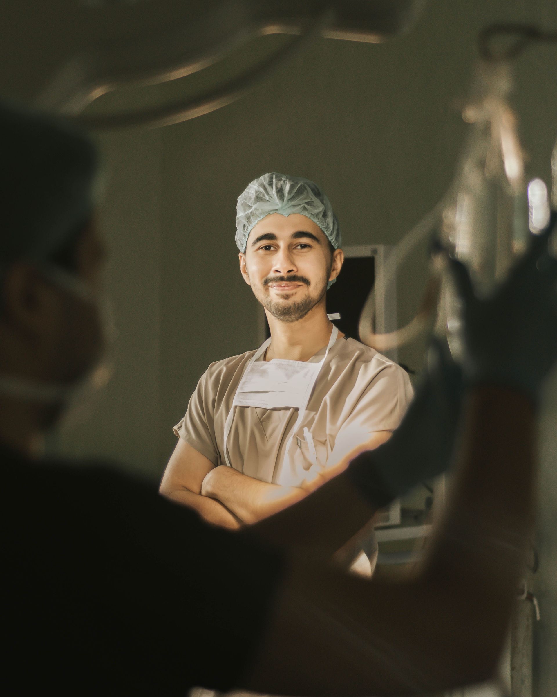 Person in a hairnet and apron stands with arms crossed, smiling in a kitchen or food prep setting.