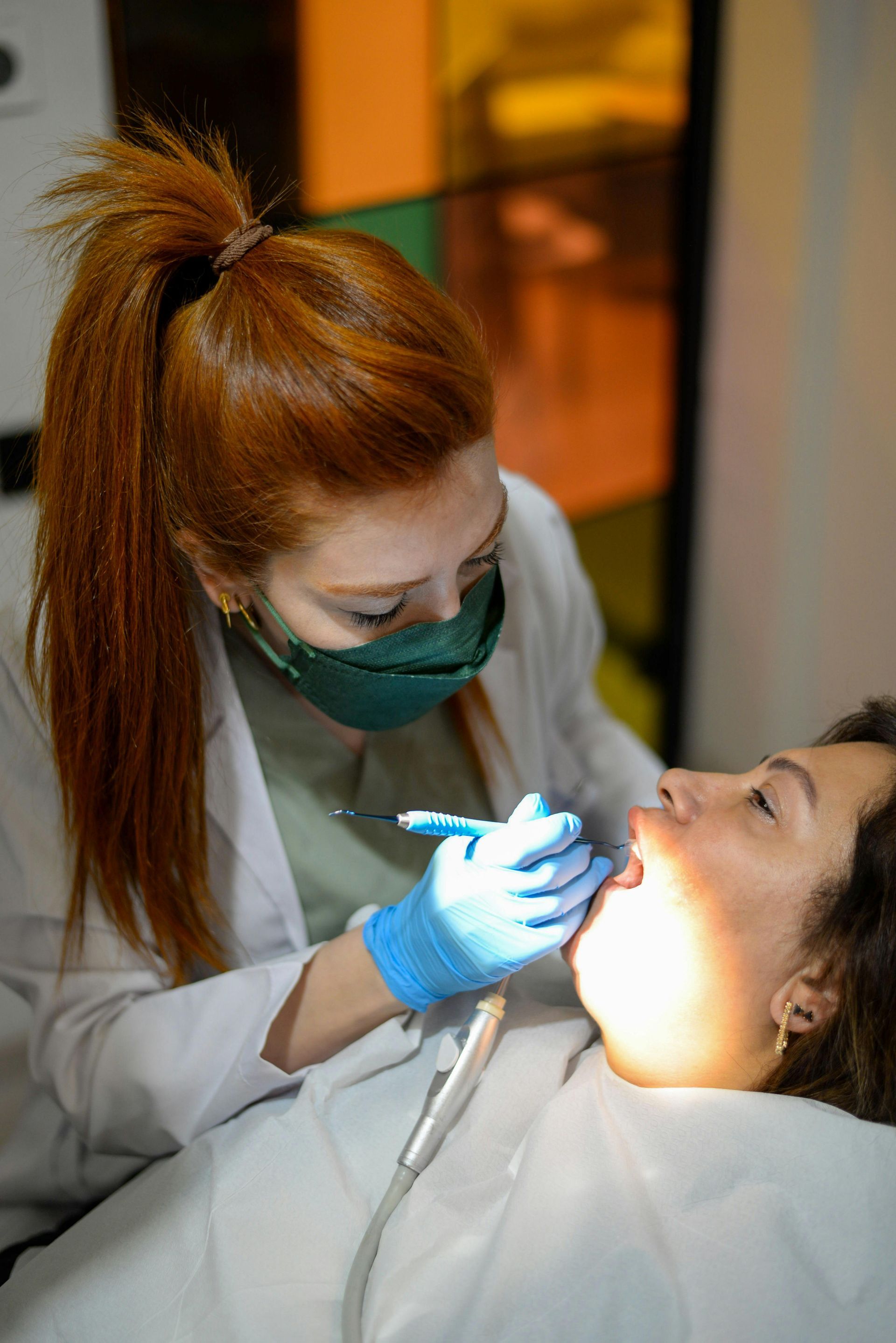 Dentist wearing mask examines a patient’s teeth with a bright light in a clinic