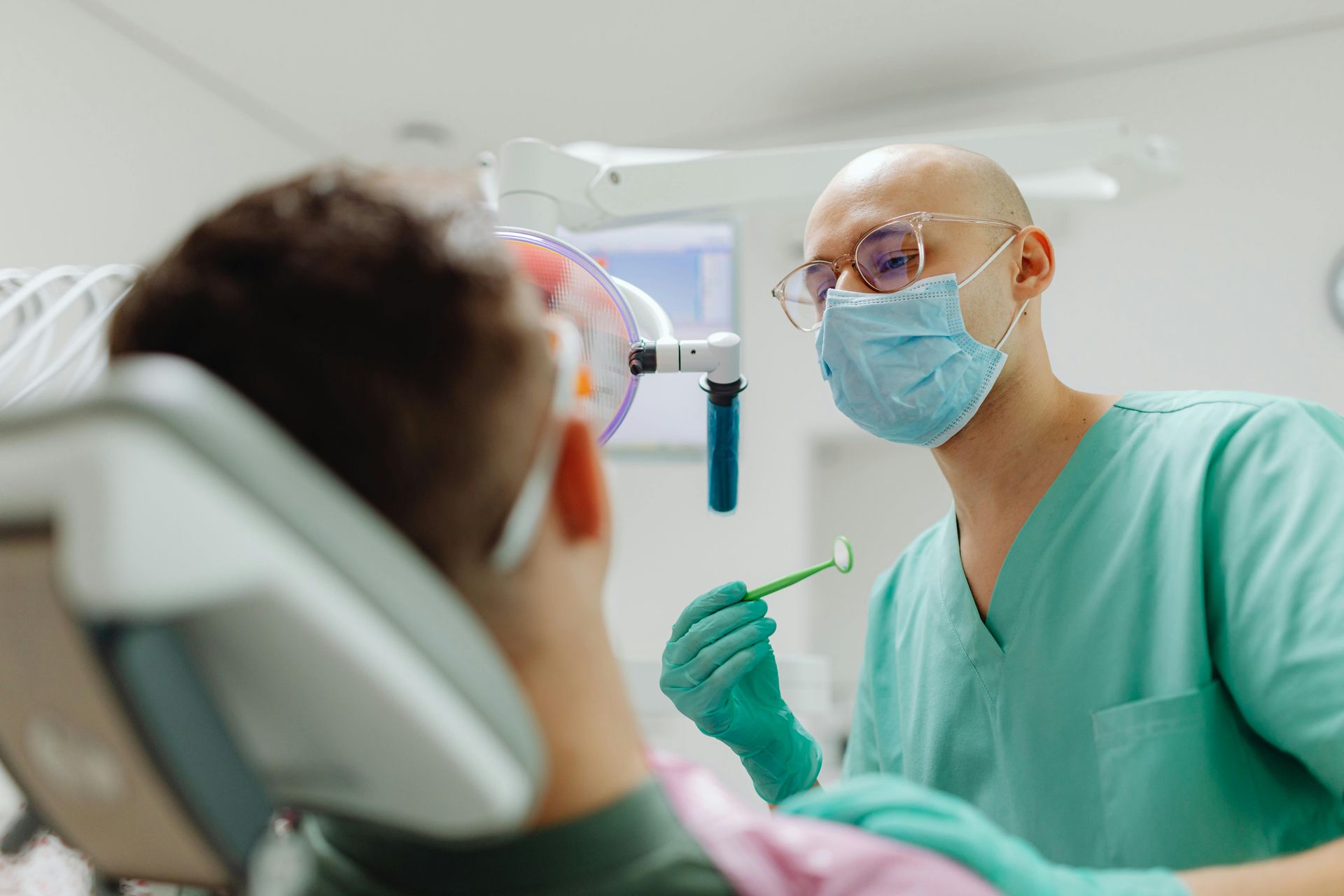 Dentist examining a patient in a dental chair, wearing a mask and gloves in a bright clinic