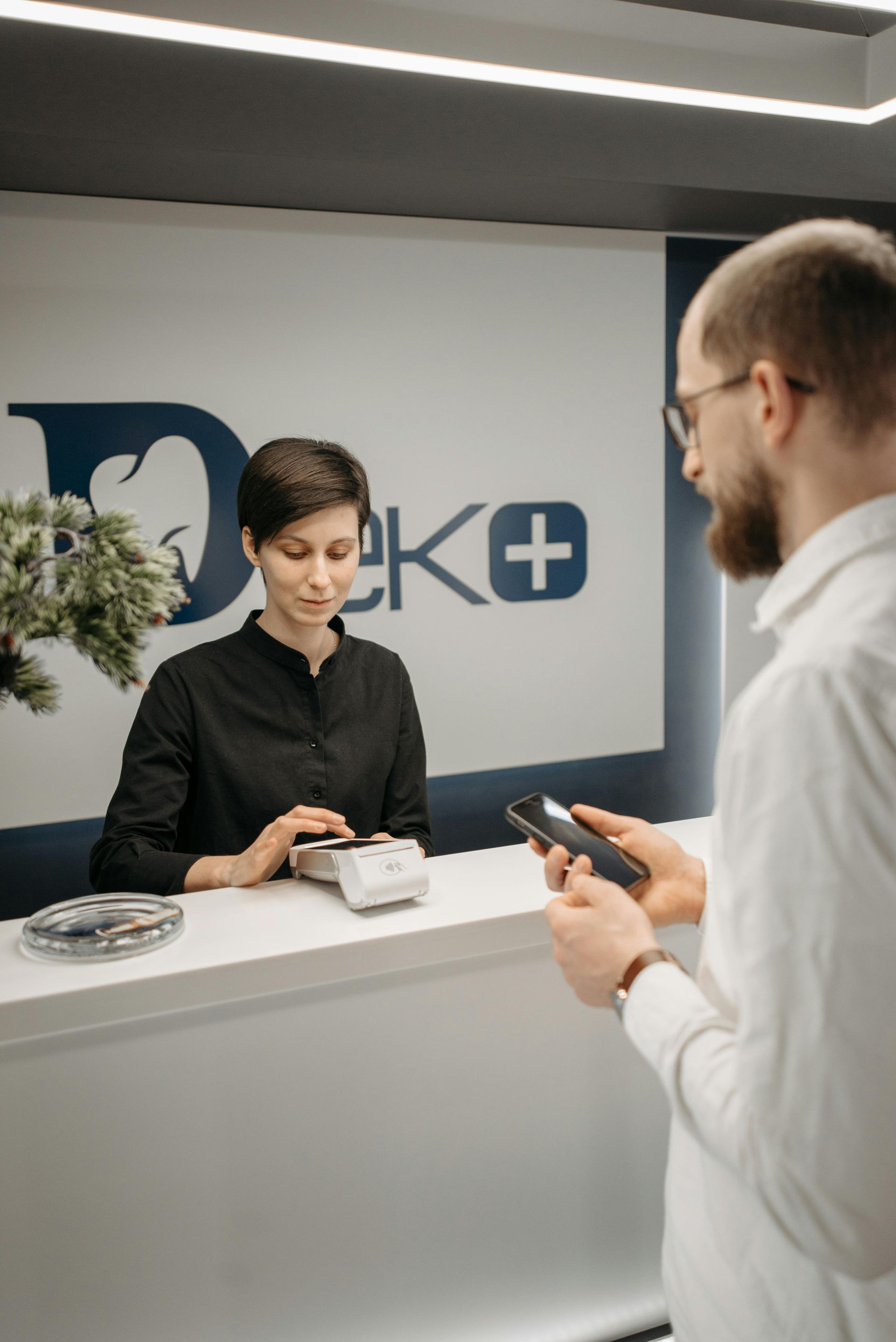 Reception desk with a clerk assisting a customer holding a smartphone in a modern office lobby
