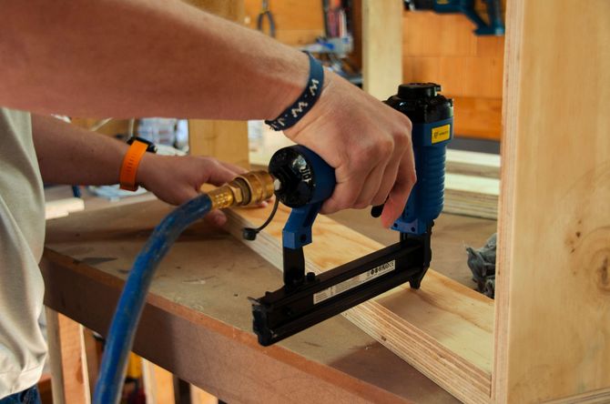 Hands using a blue nail gun to fasten wood in a workshop