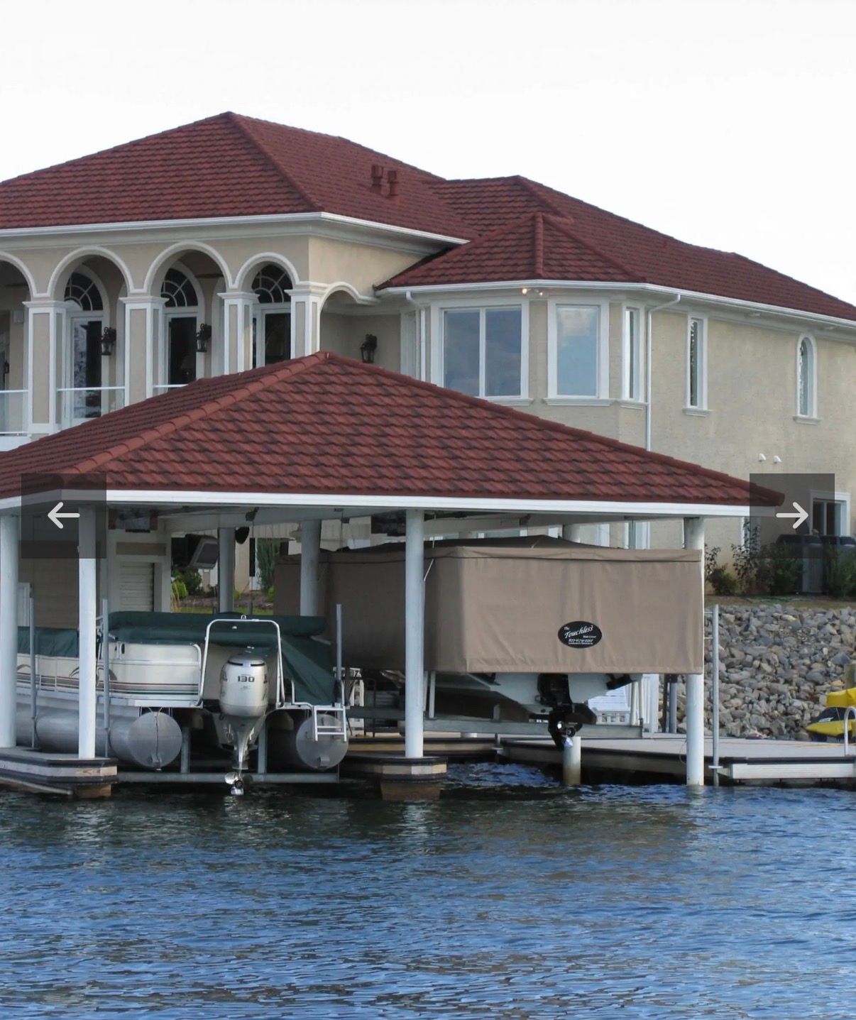 Waterfront house with red-tiled roof and boat dock over blue water