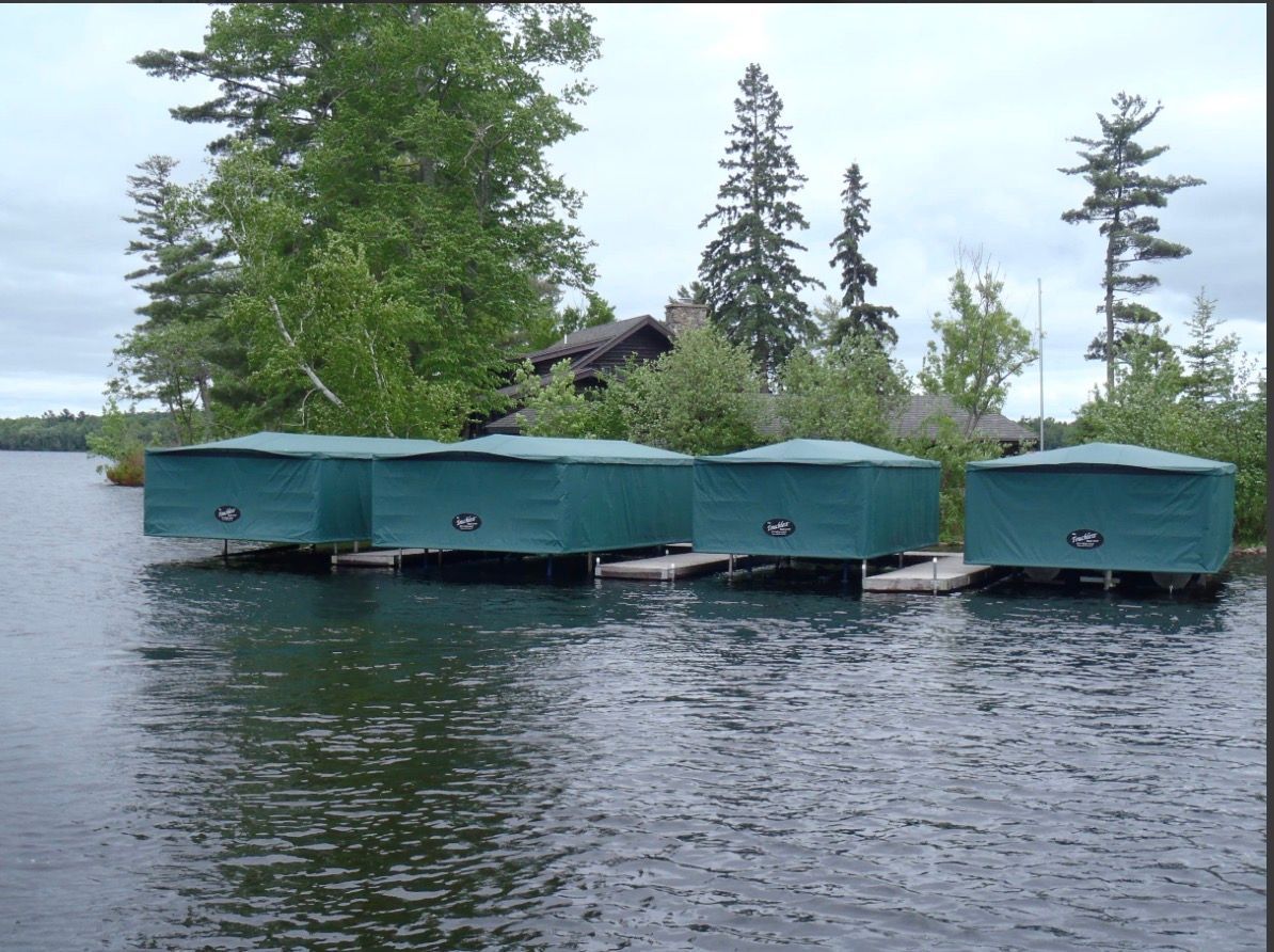 Green floating boathouses on a calm lake with trees and cloudy sky in the background