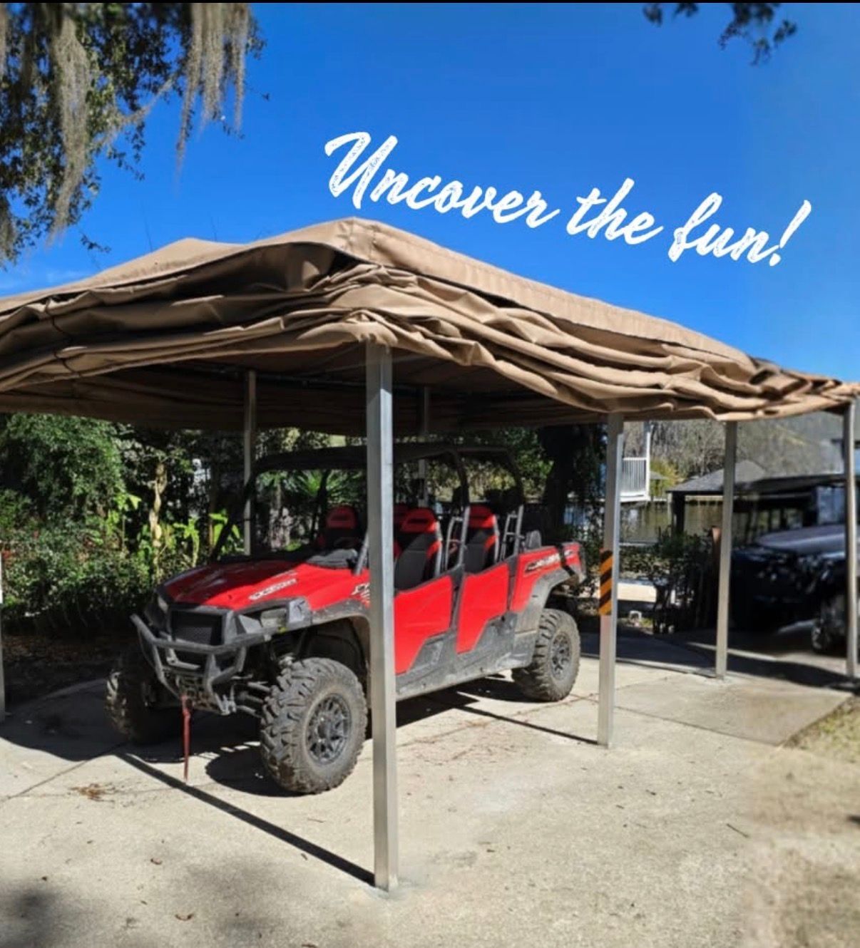 Red off-road buggy parked under a tan canopy beside a black SUV, with “Uncover the fun!” text overhead.
