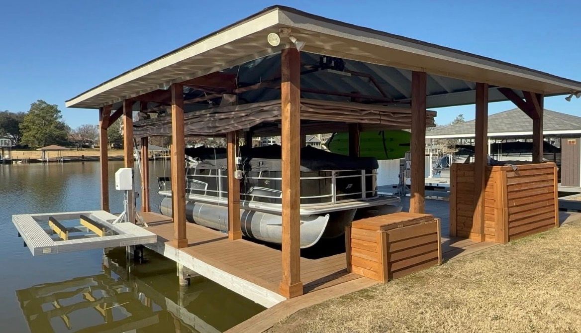 Wooden dockside pavilion with a boat lift and seating beside calm water under a sunny sky