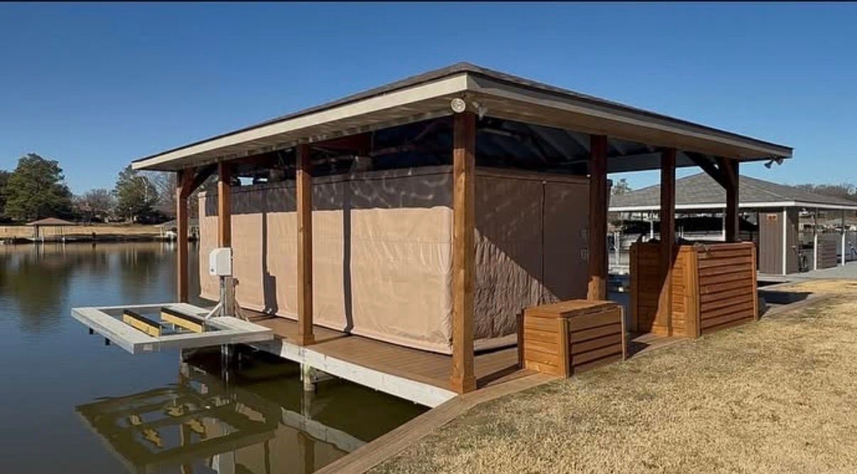 Floating wooden cabin on a pond, with a covered deck and grassy shore beside it.