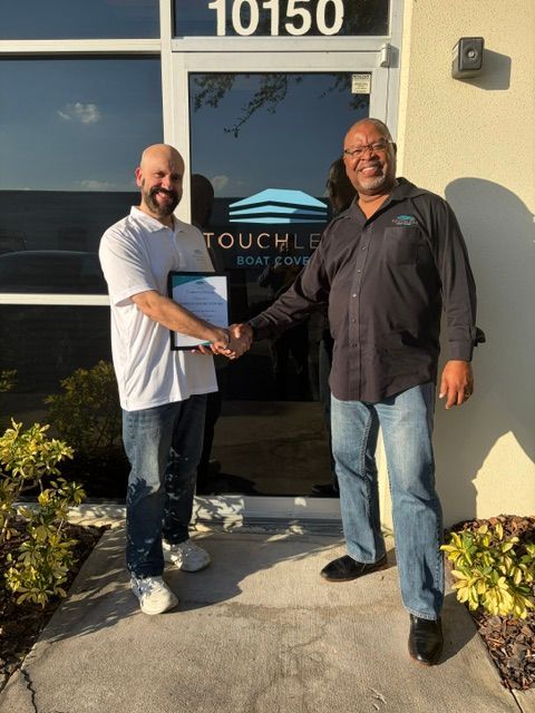 Two men shaking hands outside a building entrance with the number 10150 and a sign reading TOUCHLEAF.