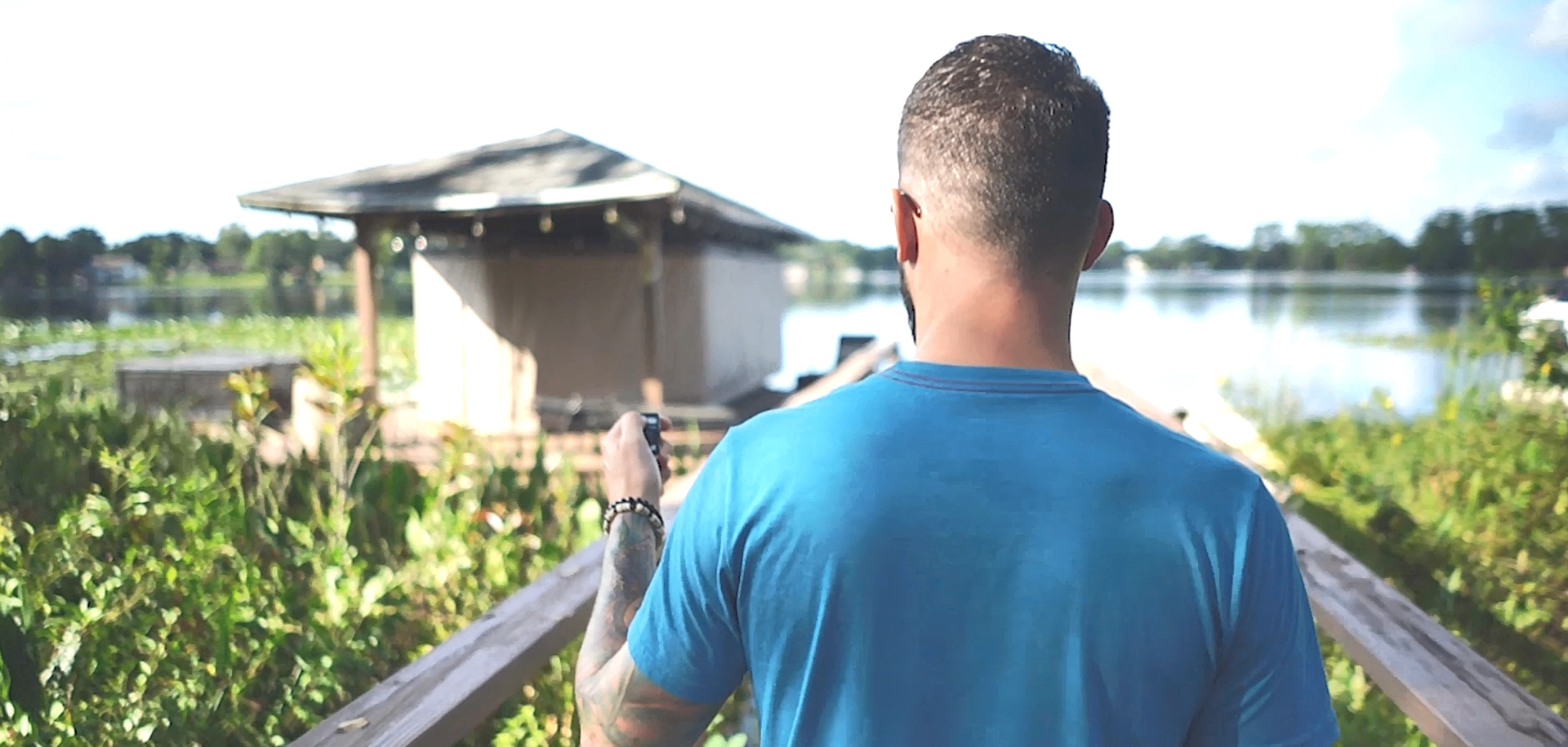 Man in blue shirt walking on a wooden path toward a lakeside cabin