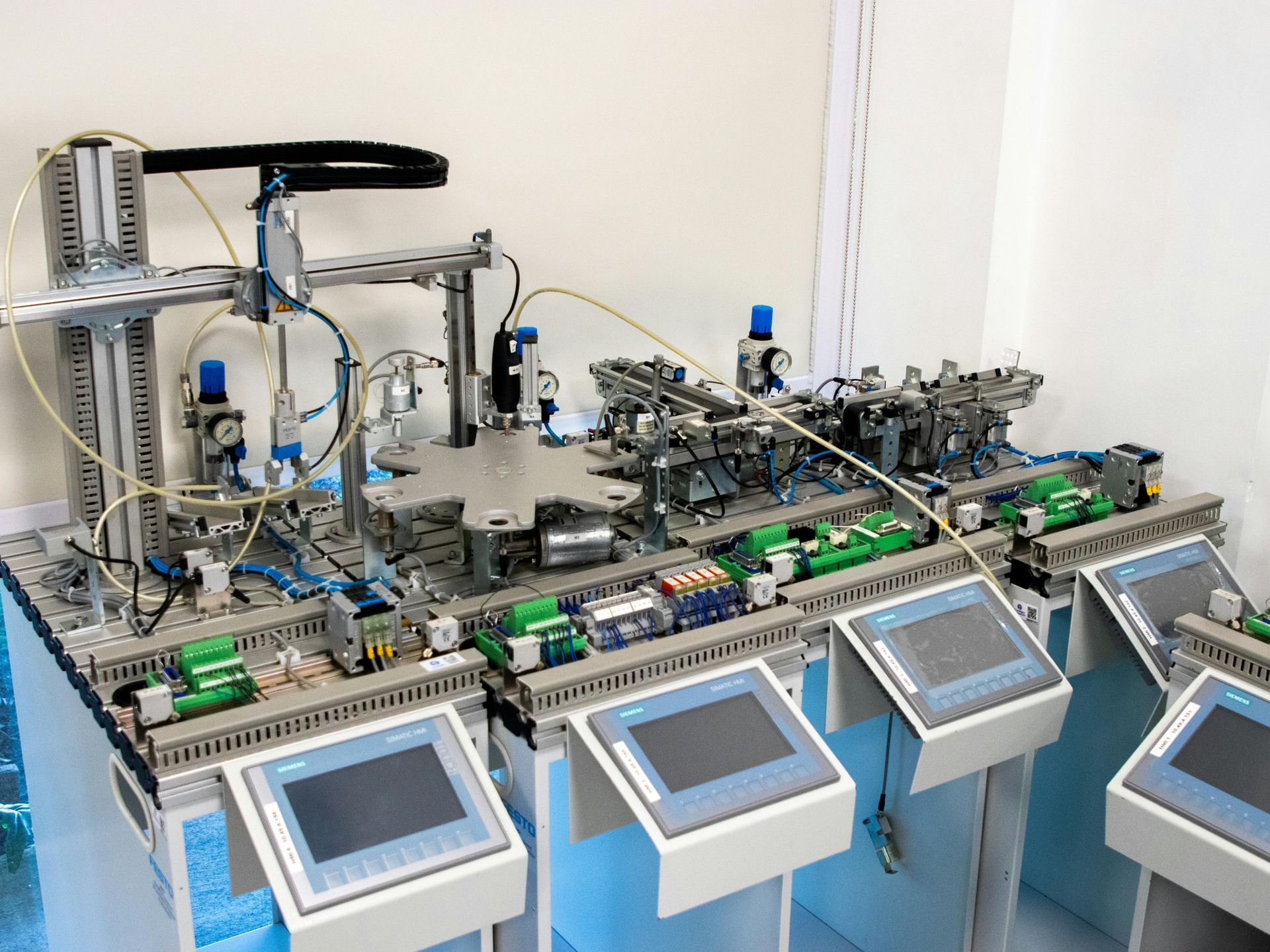 Automated industrial assembly line with multiple touchscreen control panels in a white lab setting