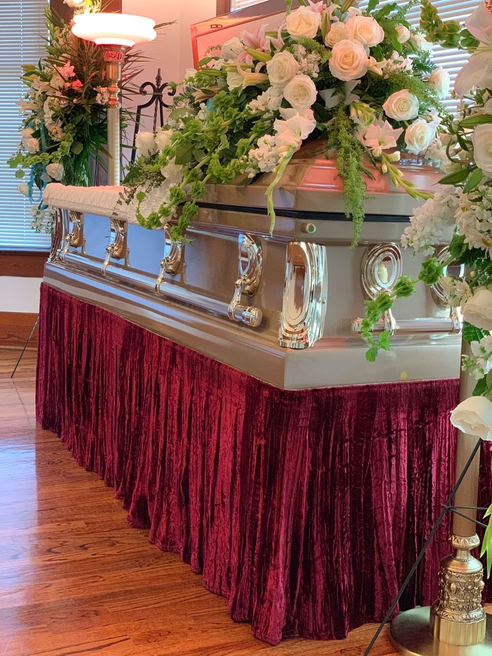 Floral-adorned buffet table with burgundy skirt in a wood-floored banquet hall